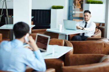 Arkadan görünüş meşgul çalışanın iş ortağı smartphone güzel küçük kahvehane, çalışırken konuşurken yan masada oturan ve ilgi ile gözü üstünde orta yaşlı meslektaşı