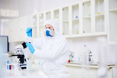 Gaz maskesi ve zehirli sıvı iç arka plan üzerinde modern laboratuvar mikroskop altında eğitim coverall giyen erkek kimyager