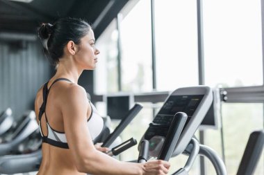 Yan görünümü kullanarak eliptik makinesi büyük pencere karşı modern spor olarak çalışma sırasında egzersiz güzel sportif kadın portresi