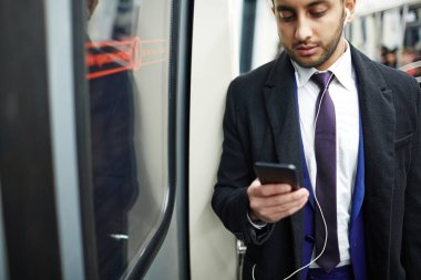 Müzik ve metin mesajları dinlemek için smartphone kullanarak metro treninin penceresinde beklemedeyiz genç Orta Doğu iş adamı