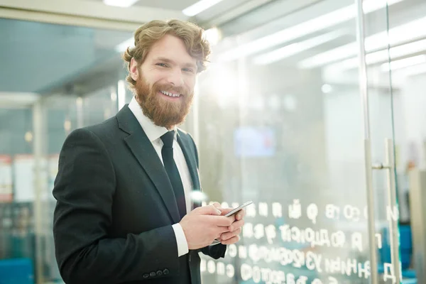 Retrato Jovem Empresário Barbudo Sorrindo Para Câmera Segurando Smartphone Escritório — Fotografia de Stock