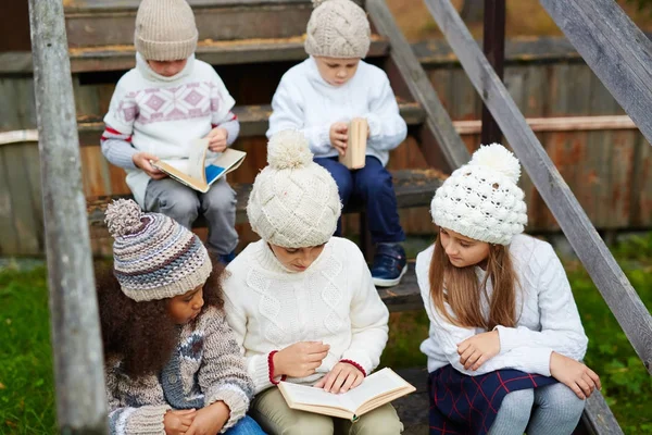 农村的孩子们在户外玩耍 坐在乡村小屋的木制台阶上 看书都穿着类似的针织衣服 — 图库照片