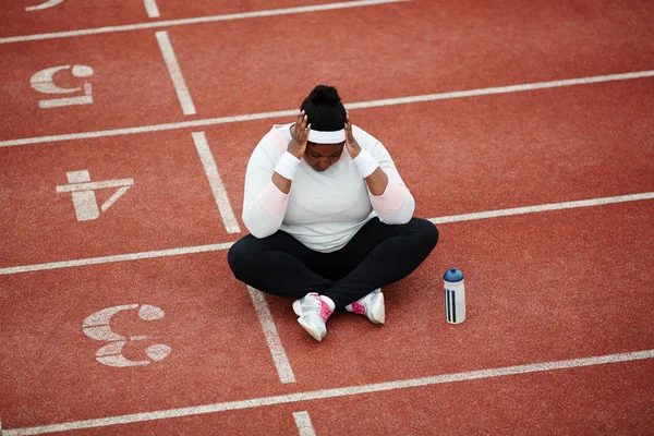 Utmattad Överviktiga Afrikansk Kvinna Skräddarställning Sitter Nära Startlinjen Löparbana — Stockfoto