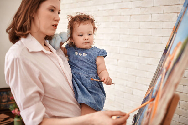 Portrait of young mother painting picture in art studio with baby girl