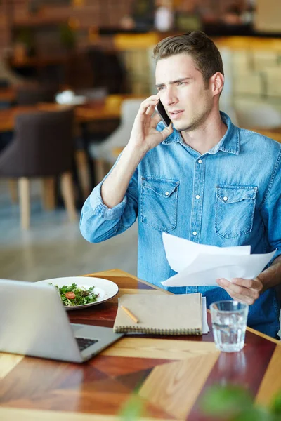 昼食時に携帯電話で誰かをコンサルティングの論文と若い男 — ストック写真