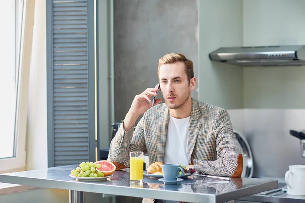 Junger Mann Sitzt Serviertisch Und Telefoniert Der Küche Mit Smartphone — Stockfoto