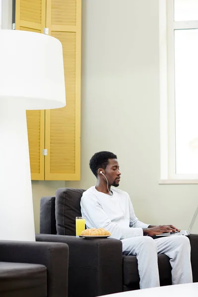 美国集中的非洲裔美国人的个人资料视图玩电脑游戏 而在家里度过慵懒的周末 在扶手上开胃早餐 — 图库照片