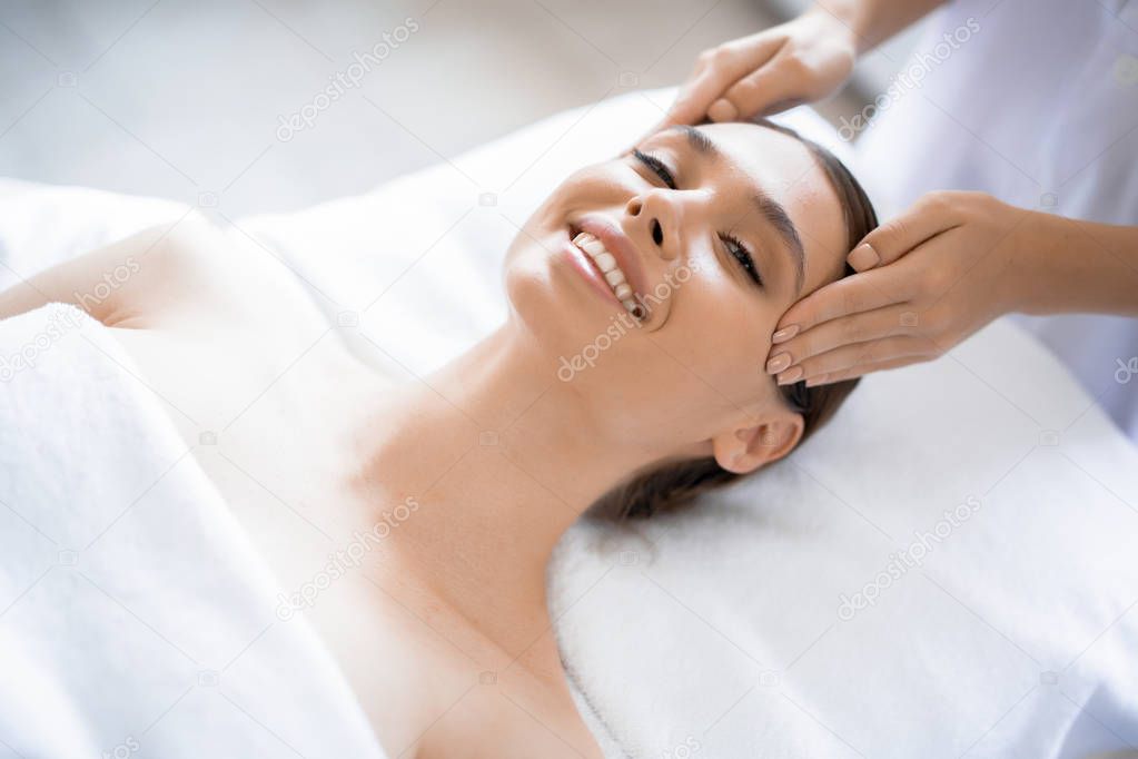 Young smiling woman enjoying facial spa massage in beauty salon