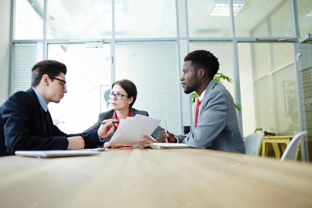 Talented team of white collar workers wearing suits having working meeting at spacious boardroom and sharing ideas concerning start-up project