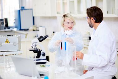 Mümkün tartışırken koruyucu gözlük takıyor yetenekli microbiologists gurup modern laboratuarda test tüpleri tutan kadın meslektaşım bir araya süre başarısız deneme için önde gelen neden olur.