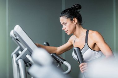 Yan görünümü eliptik makinesi kullanarak modern spor olarak yoğun çalışma sırasında egzersiz güzel sportif kadın portresi
