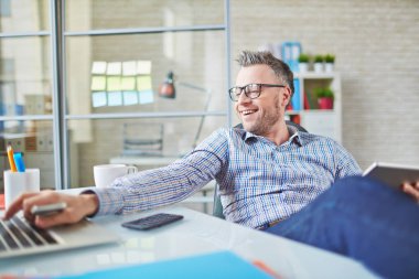 İyimser orta yaşlı işadamı kolay iş modern cihazlar ile o dizüstü bilgisayarda yazarak ve ofis masasında oturan zevk