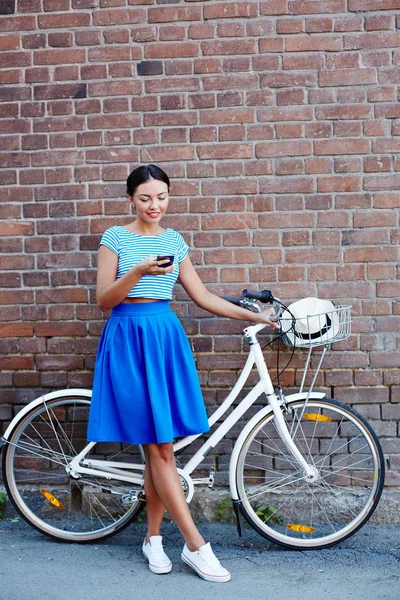 かわいい女の子彼女の自転車で立っている間メッセージング — ストック写真