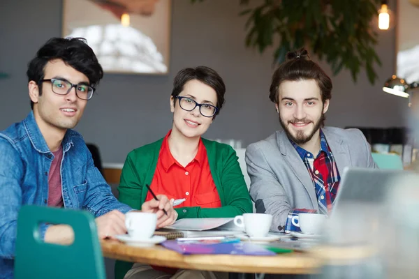 三有创意的人穿着商务休闲微笑看着相机 在会议期间工作在表 — 图库照片