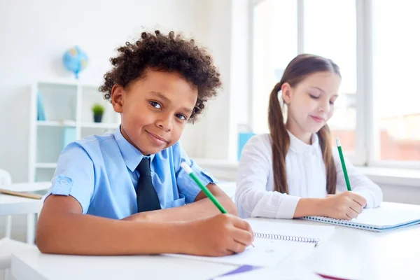 アフリカ民族背景上に同級生のコピーブックに鉛筆で描画のかわいい男の子 — ストック写真