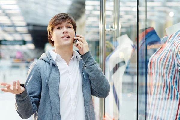 Mobile guy speaking by smartphone while standing by shop-display in the mall