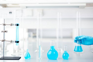 Satır farklı cam şişeler ve test tüpleri ile renkli kontrollerimiz sıvı test araştırma modern laboratuvar, eldivenli elini tutan bir tanesi tablo için hazır