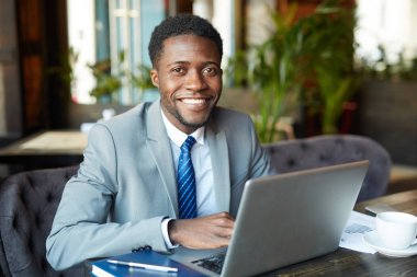 resmi giyen işadamı neşeyle kafede dizüstü bilgisayar ile çalışırken kameraya bakarak gülen uygun