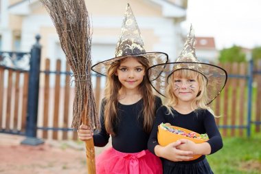 Cute little witches with broom and treats on background of house clipart