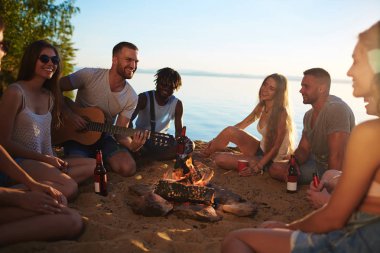 Yaz akşamı Gölü kamp ateşi etrafında oturan dostu genç grup