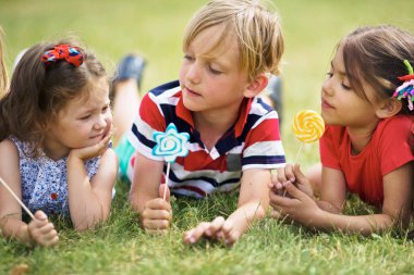 Park yeşil çim üzerinde yalan, lolipop tutan ve harika yaz gününde sohbet şirin çocukları yakından görmek