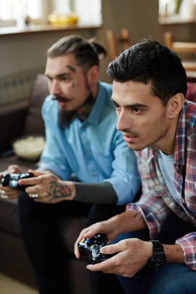 两个现代成年男子的肖像 其中一个严重纹身 享受视频游戏比赛和手持无线控制器 而坐在沙发上的客厅 — 图库照片