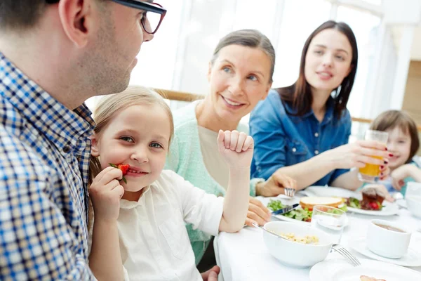 かわいい女の子の近くで彼女の家族と一緒に朝食の新鮮なイチゴを食べる — ストック写真