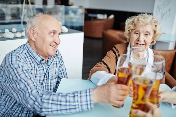 ビールのグラスを一緒にカーンカーンながらきれいな女友人を見て歯を見せて笑顔でハンサムな年配の男性のプロフィール — ストック写真