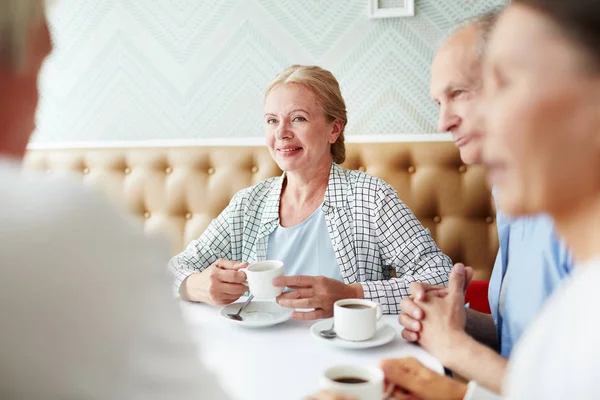 Cheerful senior friends enjoying each others company while having tea party at cozy small cafe with stylish decor