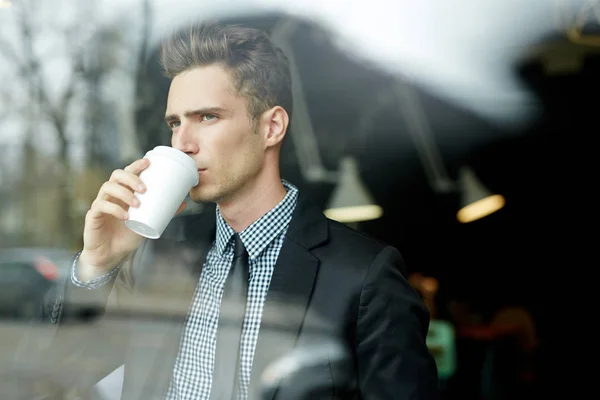 オフィス ロビーに立っていると紙コップからコーヒーを飲みながら窓の外見ている思いやりのある青年実業家のウエスト アップ肖像画 — ストック写真