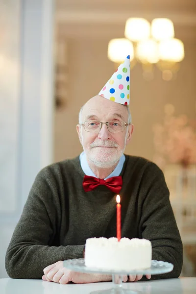 坐在餐桌上带着生日蛋糕 戴着派对帽的漂亮老人的肖像 微笑着愉快地拍照 — 图库照片