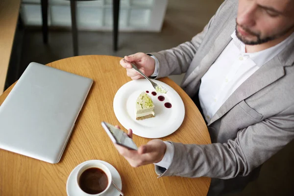 カフェでおいしいデザートやテキスト メッセージを食べるモバイル実業家 — ストック写真