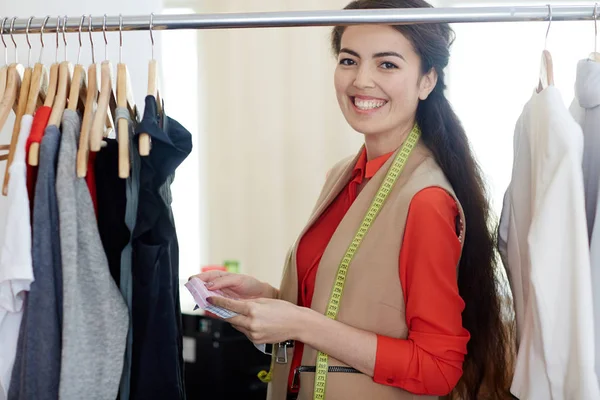Happy young fashion designer standing by clothes rail