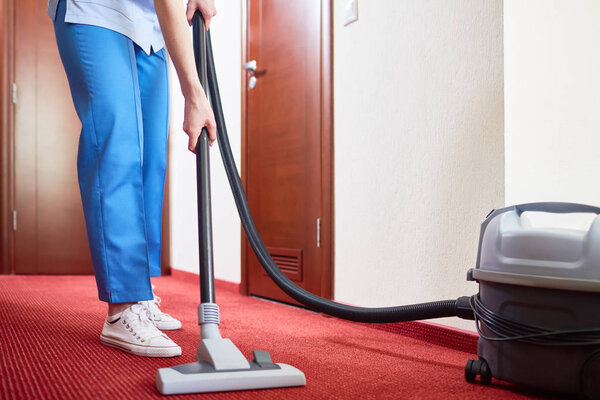 Housekeeper cleaning carpet with vacuum-cleaner
