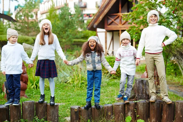 不同年龄的快乐孩子们在绿色的乡间玩得开心 站在木柱子上 手里拿着类似的白色针织衣服 — 图库照片