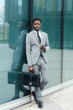 Evrak Çantası'nı ayakta camsı duvarla modern ofis binası ile iyi giyimli adam