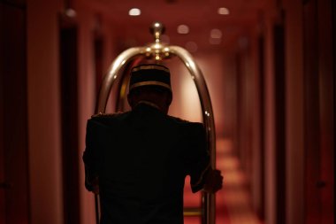 Bagaj arabası ile otel koridor boyunca hareketli hizmetçi arkadan görünüş