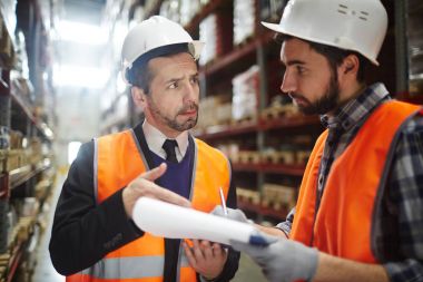 Portrait of warehouse worker talking to supervising manager while doing inventory control in entrepo clipart