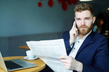 Yakışıklı genç işadamı tarafından smartphone kafede Gazete okurken konuşan portresi