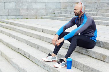 Genç adam merdivenlerde oturan ve kulaklık müzik dinlemek giyim