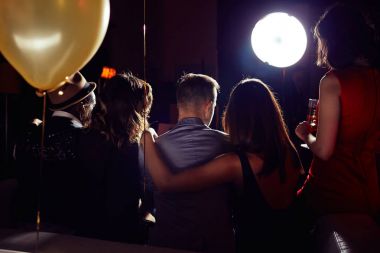 Arkadaş grubu evde parti, onlar kanepede oturan ve şampanya içmek dışarı asılı iki genç çiftlerin arkadan görünüm