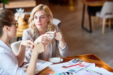 Kahvehane, gayri resmi çalışma toplantısı: çekici genç moda tasarımcıları üretken sahip proje tartışma sırasında masada oturan ve güzel kokulu kapuçino, arka plan bulanık içme