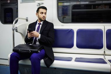 Müzik dinlemek için smartphone kullanarak metro treninin çalışmaya commuting genç Orta Doğu işadamı portresi