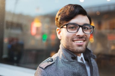 Kameraya bakarak gözlük gülümseyen genç adam