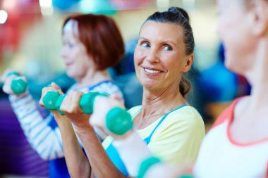 Dambıl ve spor salonunda egzersiz arkadaşları ile gülen Olgun kadın