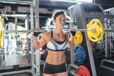 Büyük ağır bar omuzlarında modern spor salonunda tutan halter egzersiz yaparak spor giyim giymiş güzel tabaklanmış kadın portresi
