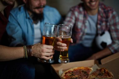 Evde toplantı, karanlık odada bira gözlük ile toasting ve futbol maçı televizyonda izlerken pizza yemek kanepede oturan arkadaşlar grup portre portre