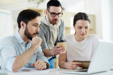 Grup odaklı iş adamları modern güneşli ofiste çalışırken dizüstü bilgisayar ekranına bakarak