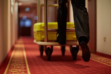 Porter moving luggage in cart down aisle covered by red carpet clipart