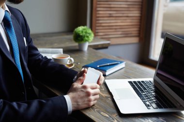 Kafede çalışan zarif modern işadamı closeup: akıllı telefon tutarak ve kahve molası sırasında uzak dizüstü arıyorum